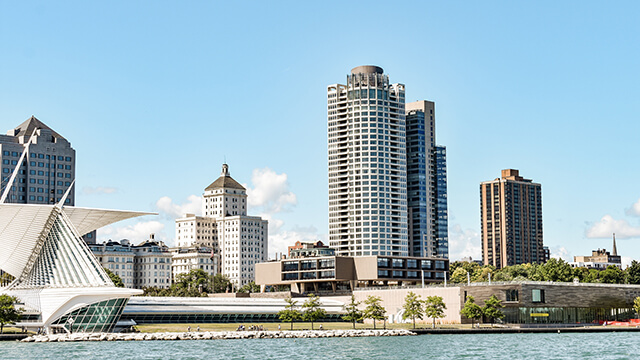 a view from the water on Lake Michigan of the Milwaukee skyline. There are tall buildings and a modern white building resembling a sailboat. 