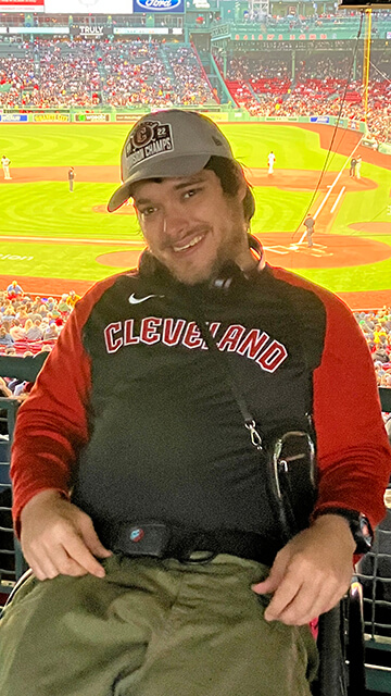 cleveland guardians fan peter knab sits in his wheelchair inside a baseball stadium with the field behind him.