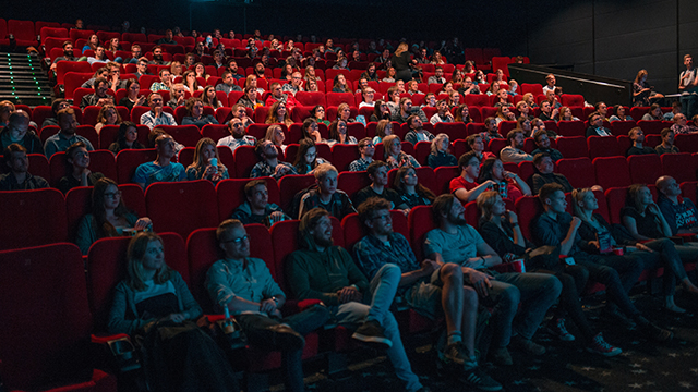 the interior of a movie theater with people sitting in red seats looking at a screen