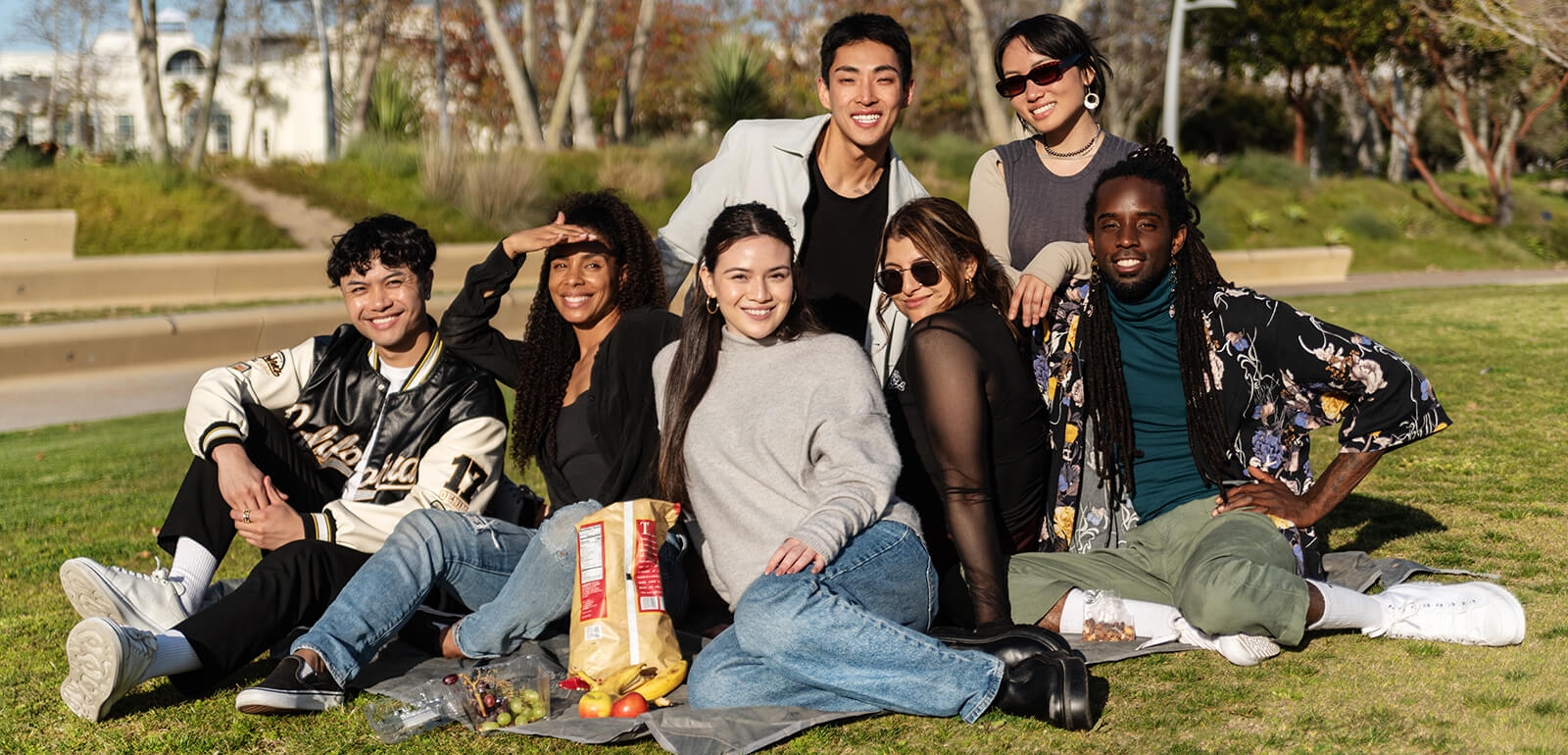 a group of young people sit together on a lawn having a picnic