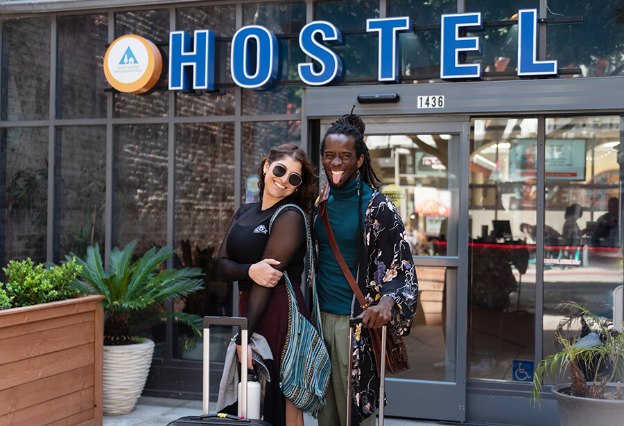 two hostellers stand playfully with luggage under a blue and orange