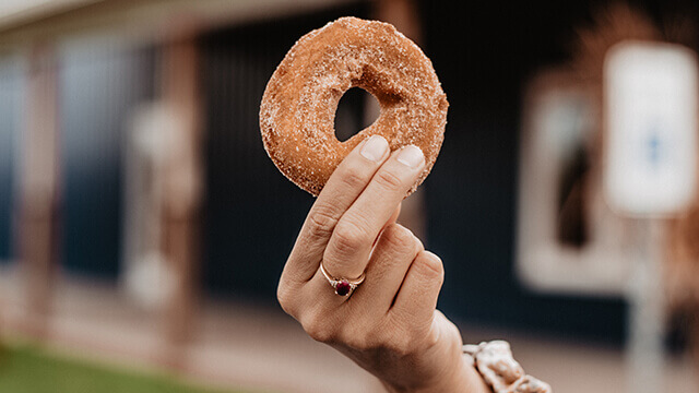 an apple cider donut covered in cinnamon sugar being held up by a woman's hand