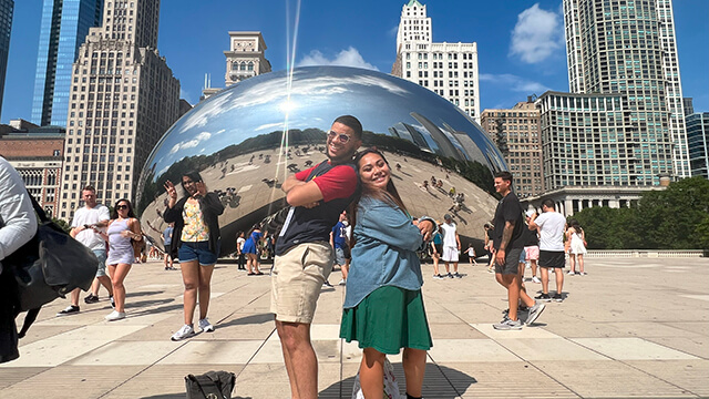 two friends stand back to back in front of the bean in Chicago