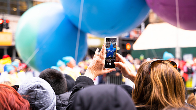 a person taking a photo at the Macy's Thanksgiving Day Parade on a phone