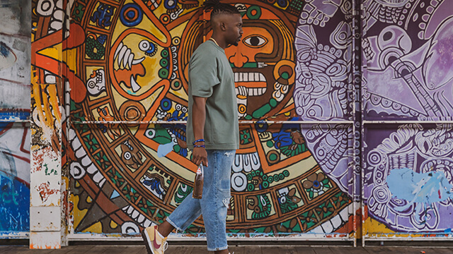 a young man walks past a mural on the wall of an L station in Pilsen, Chicago