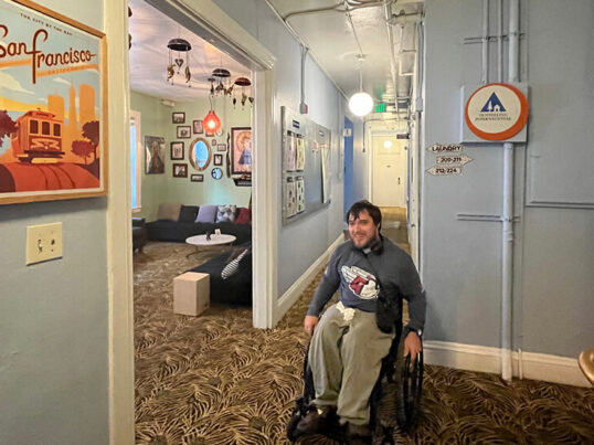 Peter Knab, who attended all 162 Cleveland Guardians games in 2023, sits in his wheelchair in the guest lounge of HI San Francisco Downtown hostel