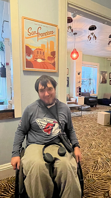 Peter Knab, who attended all 162 Cleveland Guardians games in 2023, sits in his wheelchair in the guest lounge of HI San Francisco Downtown hostel