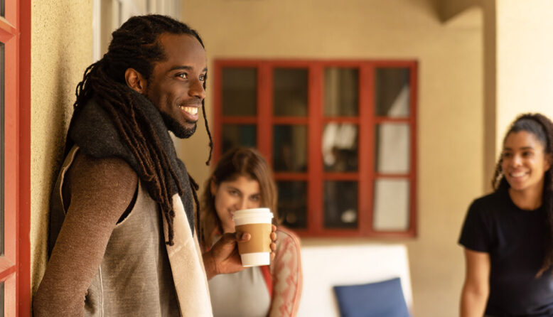 three young people in a courtyard laughing and drinking coffee