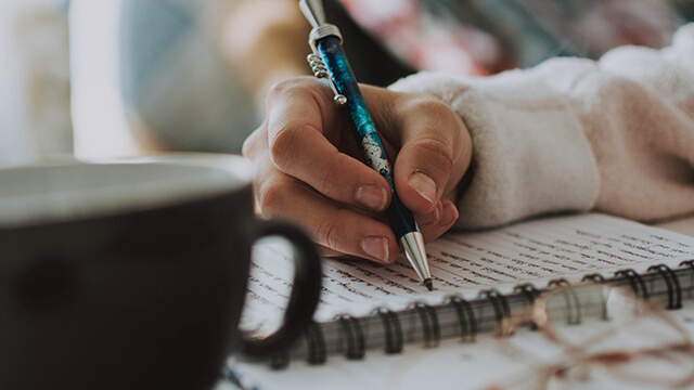 a hand writing in a journal with a coffee cup in the foreground