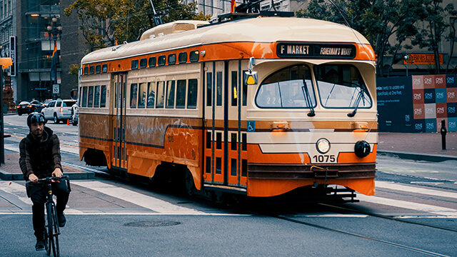 a man on a bicycle rides past an orange trolley car in San Francisco