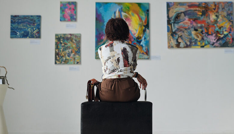 a woman sitting looking at colorful paintings on a white wall