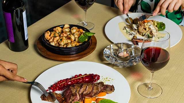 an overhead view of a multi-course dinner lad out on a table with a glass of red wine