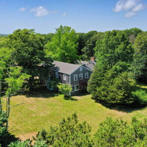 An aerial view of HI Martha's Vineyard hostel, a large grey cottage-style building surrounded by forest.