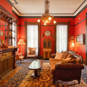 A guest parlor at HI Sacramento hostel with red walls, ornate rugs, Victorian-style furniture, and a chandelier.