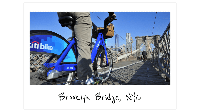 a polaroid photo of a man riding across the brooklyn bridge on a citibike bike share bicycle