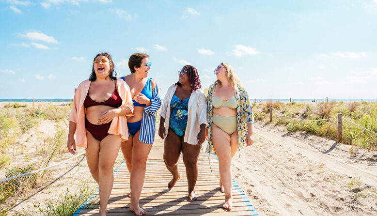 four women in swimsuits laugh as they walk down a boardwalk on the beach on Cape Cod