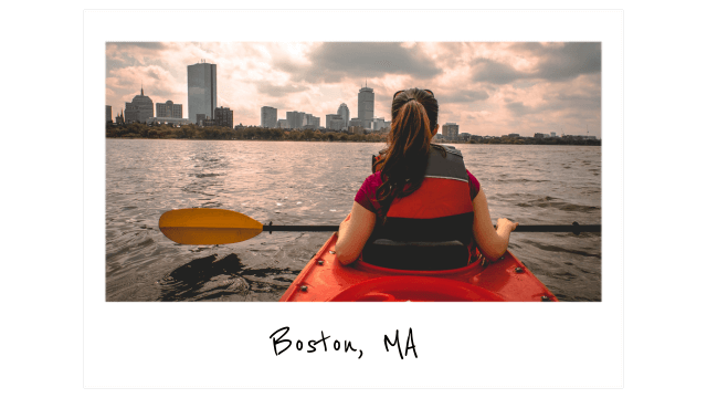 a polaroid taken from behind of a woman with a ponytail kayaking at sunset with the Boston skyline in the background