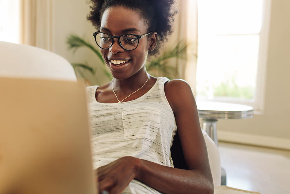 a young woman in glasses and a white tank top sits typing on a laptop
