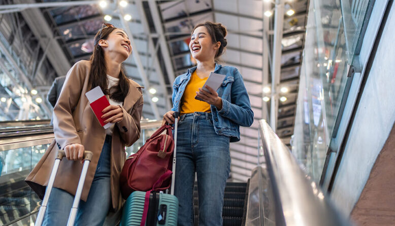 Two young women on an escalator at the airport with suitcases and passports