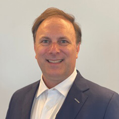 HI USA Board Chair Charles Hokanson wears a navy blue coat over a white collared shirt