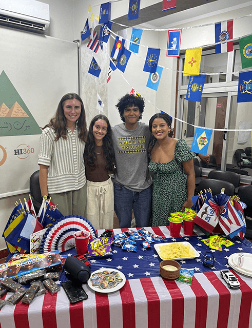 HI USA's delegation of participants for IOU Respect 2025 in Egypt pose behind a table representing the USA at the program's cultural night.