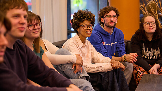 A group of college-aged students sit on sofas in the lobby of a HI USA hostel listening to their group leader going over plans for the group's day.
