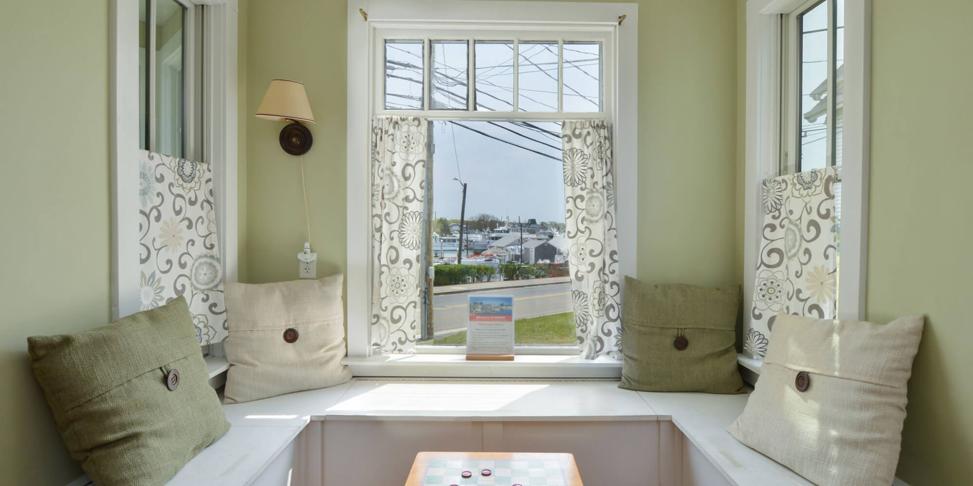 A cozy nook for guest seating near a window letting in plenty of natural light in a guest lounge at HI Hyannis hostel.