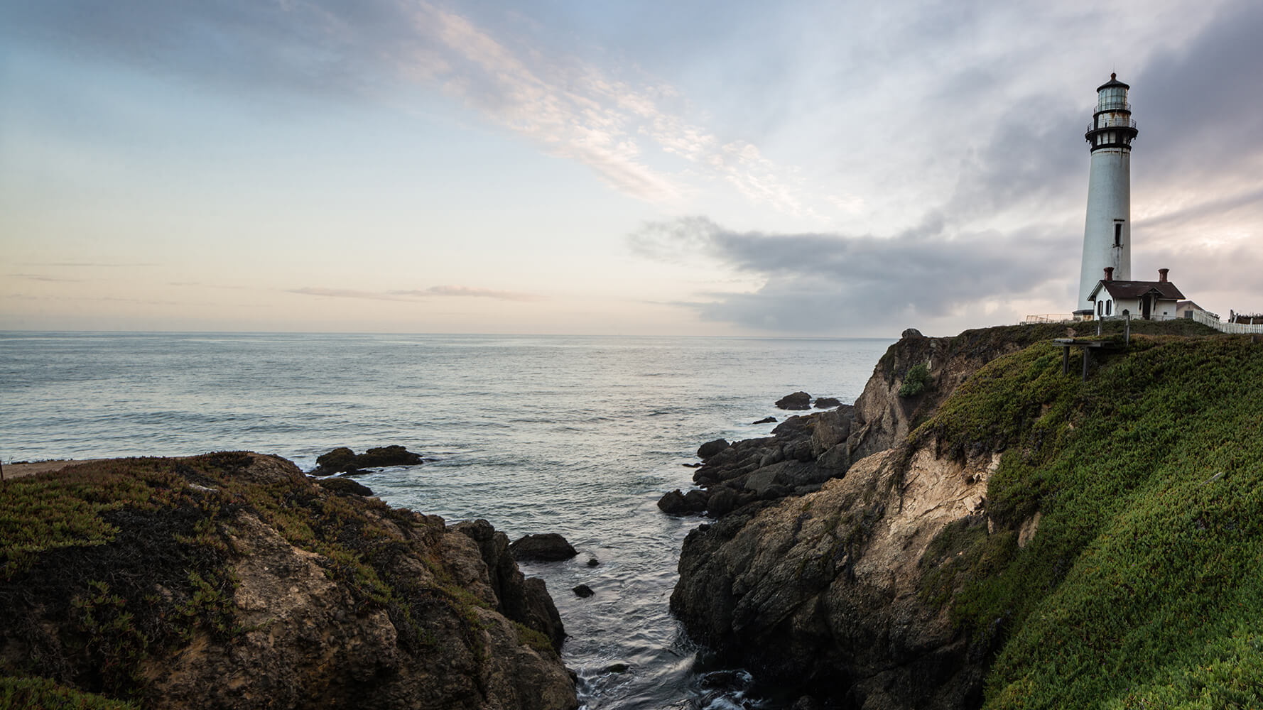 The Pigeon Point Lighthouse stands on a bluff overlooking the ocean at dusk.