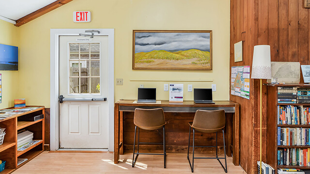 A dedicated remote work station at HI Martha’s Vineyard featuring a wooden desk with laptops, ergonomic stools, and power outlets.