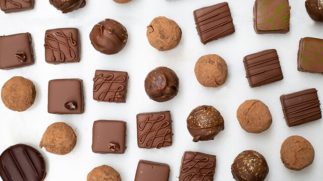 A variety of gourmet chocolate truffles, featuring milk and dark chocolate squares and rounds with elegant drizzled patterns on a white background.