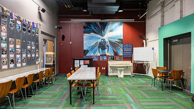The Community Room at HI Boston featuring multiple long worktables, chairs, and a whiteboard in a bright, modern space.