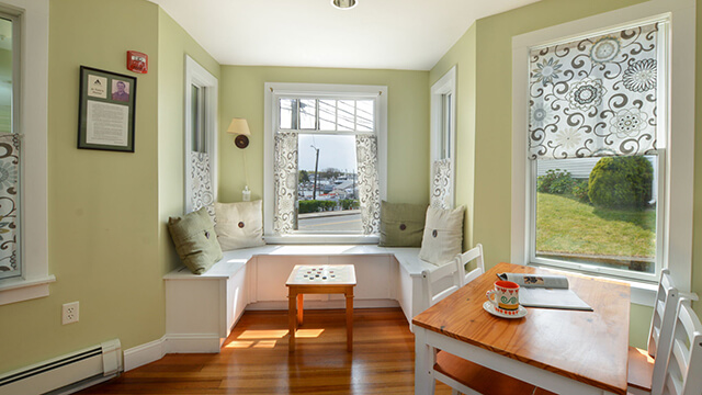 Sunlit guest lounge at HI Hyannis with a wooden worktable, window seating, and views of the street.