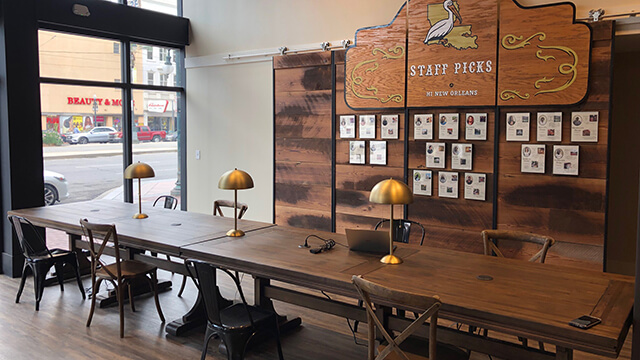 Long wooden communal worktables with brass lamps and built-in power outlets at HI New Orleans hostel.