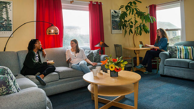 Guests relaxing and working on a laptop in the brightly colored, homey guest lounge at HI Pigeon Point Lighthouse.