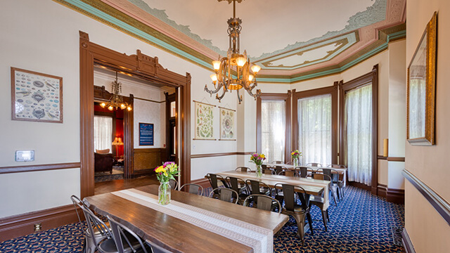 Elegant, sunlit dining room at HI Sacramento featuring long wooden tables and historic Victorian architecture.
