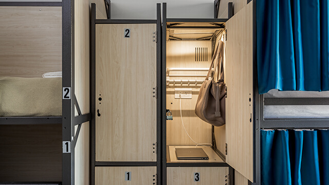 Close-up detail of a locker with charging laptop and duffle bag inside a dorm room at HI New York City hostel.