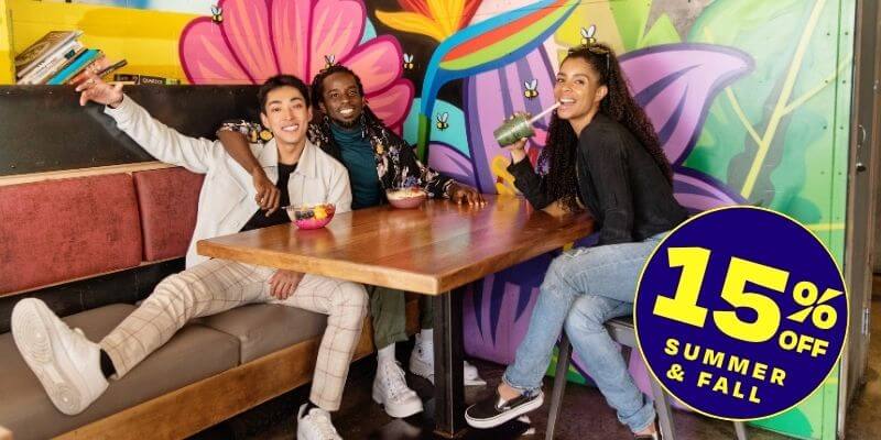 Three young travelers sit at a table with acai bowls in front of colorful murals.