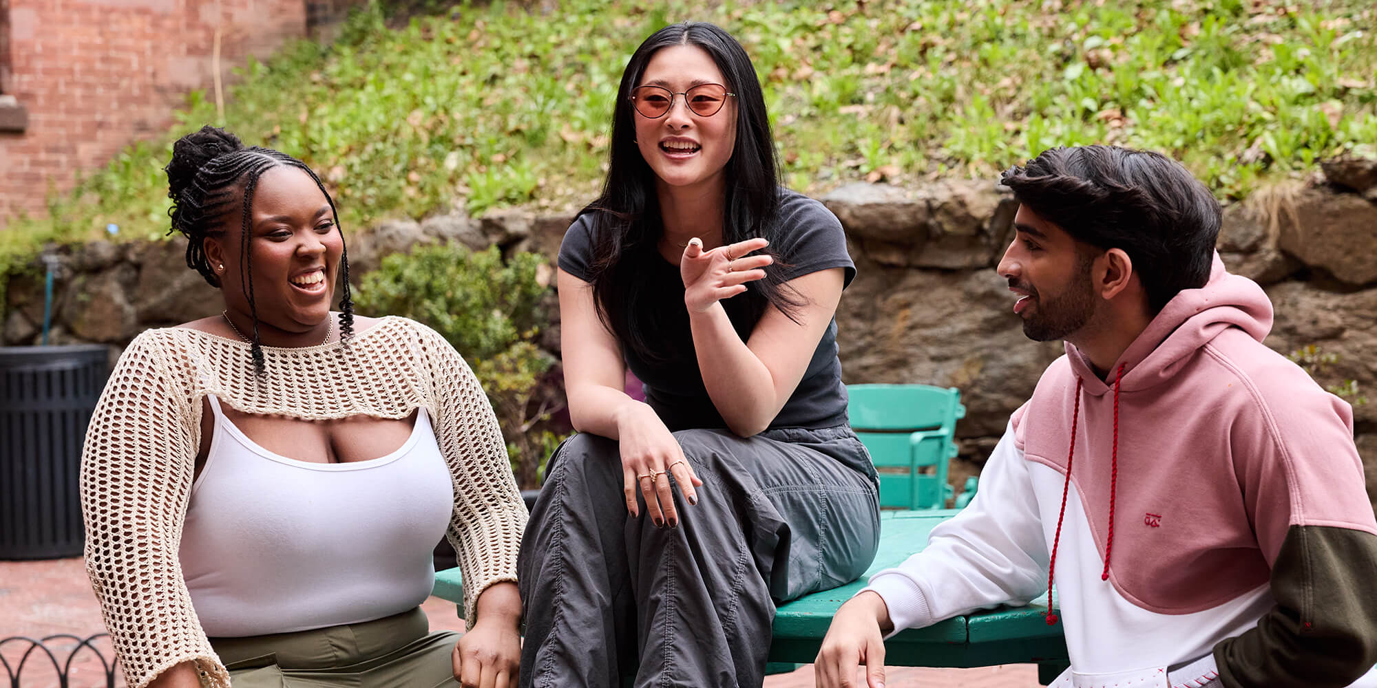 A group of three friends sits outside in the guest courtyard at HI New York City hostel talking and laughing