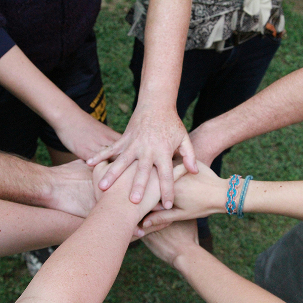Eight hands placed together in a circle over green grass