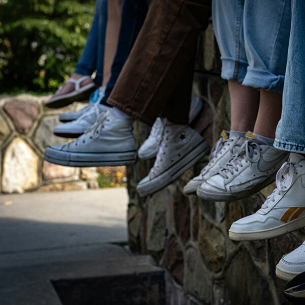 A row of legs of people sitting on a low wall wearing jeans and snekaers